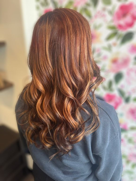Back view of long, wavy auburn hair with copper highlights against a floral wallpaper background