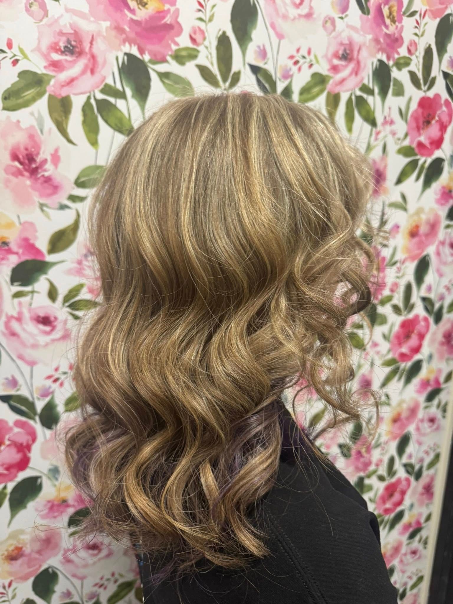 Side view of shoulder-length wavy blonde hair against a pink floral background