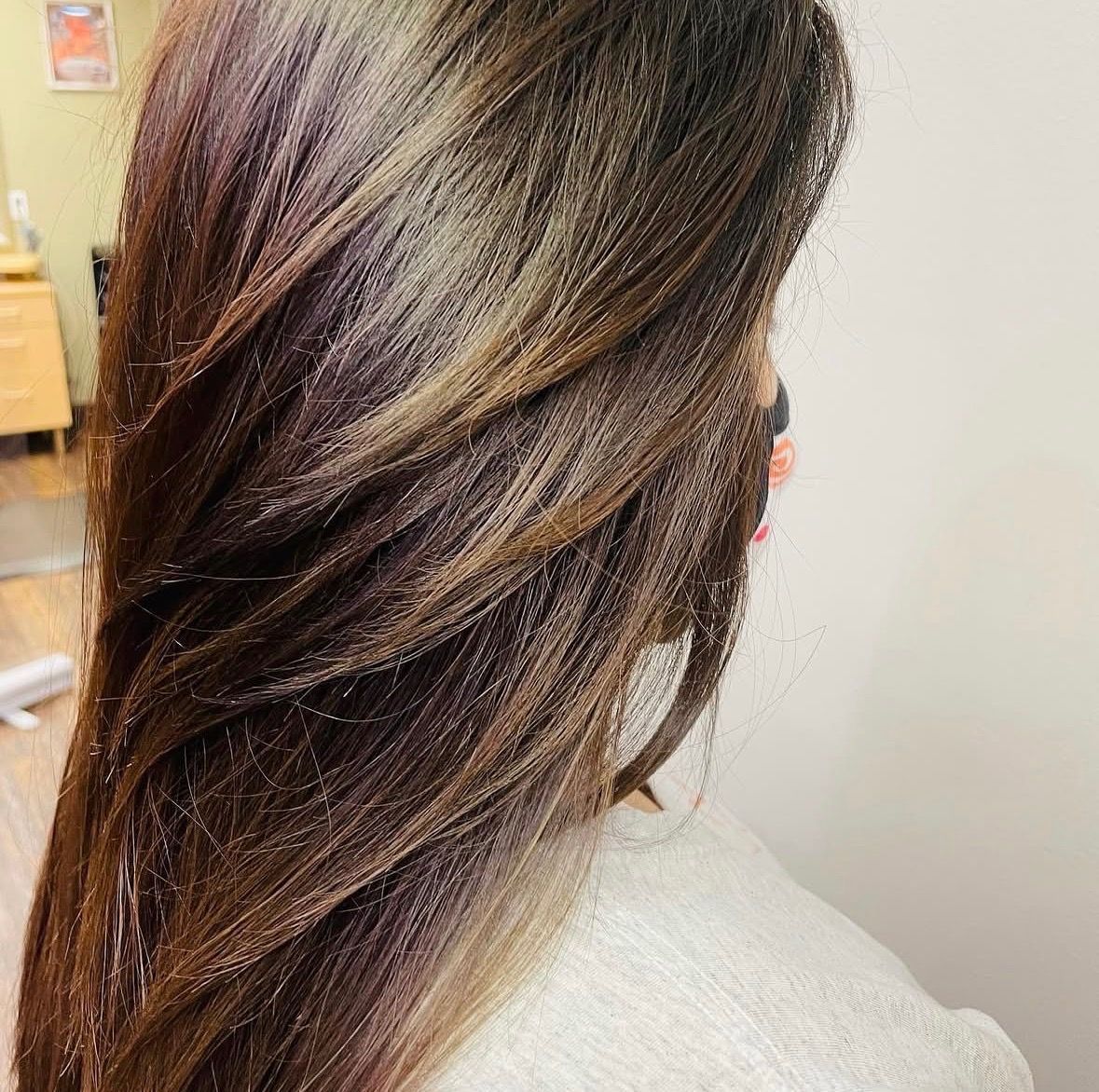 Close-up of glossy brown hair with blonde highlights, styled in a smooth twist against a light background