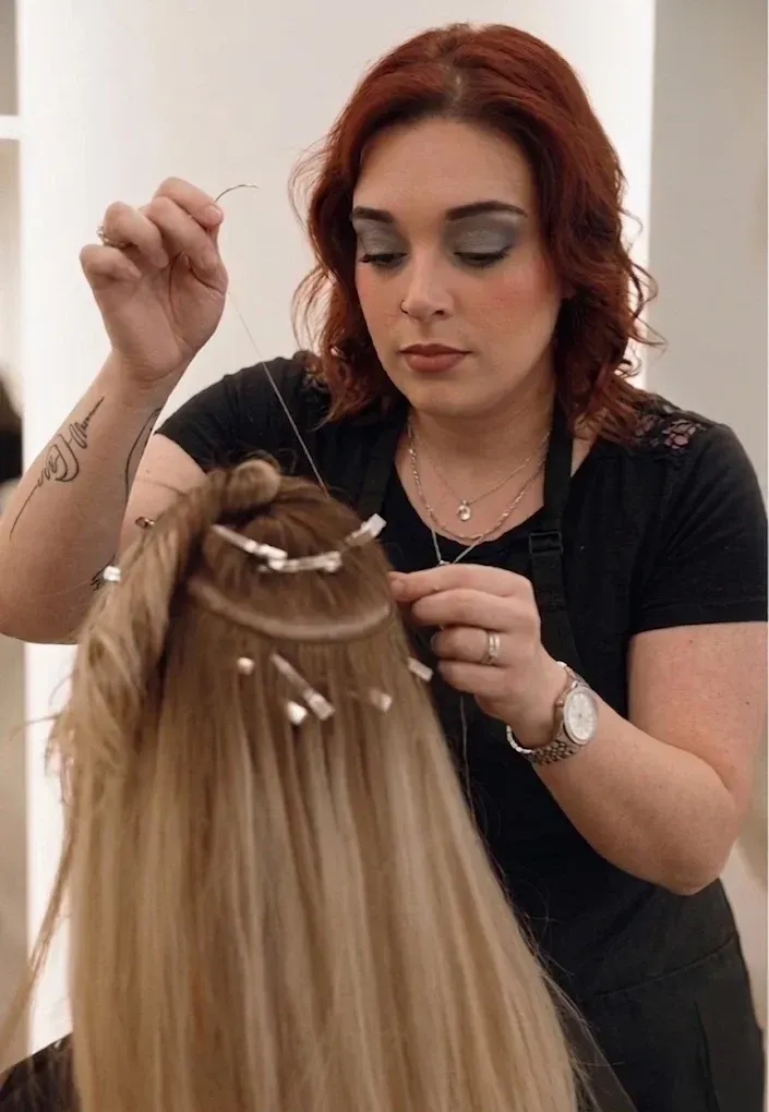 Stylist applying hair extensions to a blonde client in a salon