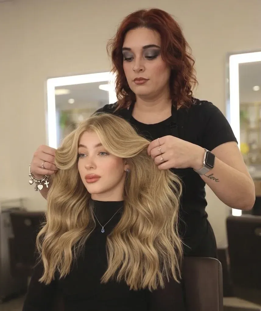 Stylist adjusting long blonde hair on a seated woman in a salon