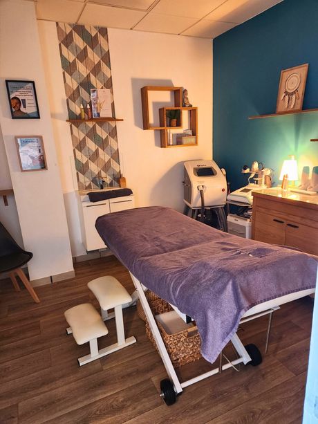 Salle de soins spa avec table de massage, équipement médical, étagères et décoration.