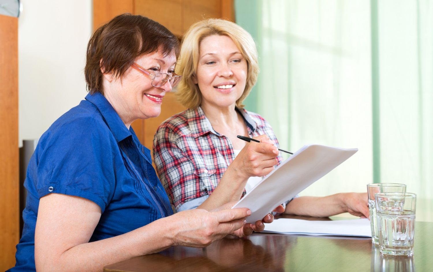 Two people sitting at a table reviewing a document together, with one pointing at the paper while smiling.