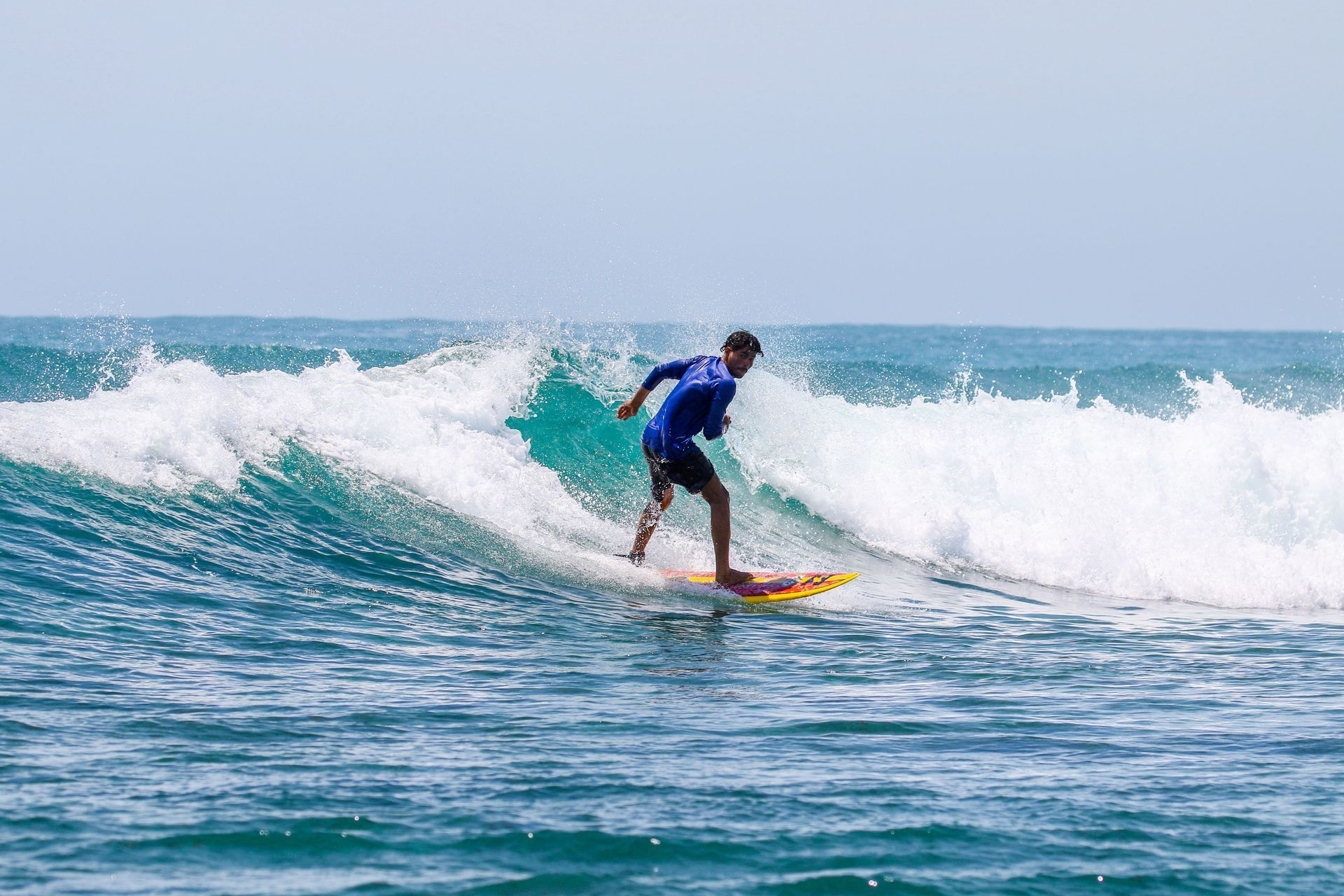 A person surfing on a turquoise wave under a cloudy, overcast sky.