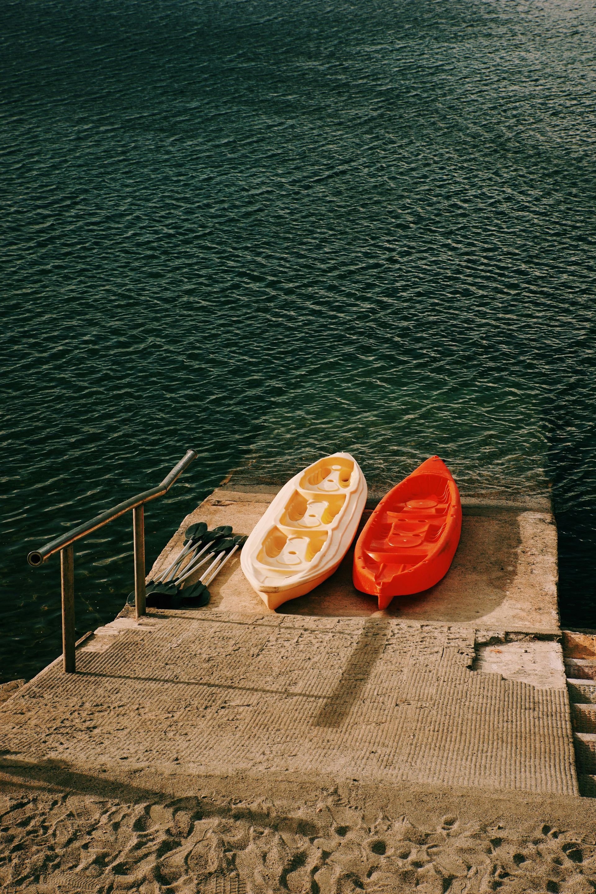 Two kayaks, one yellow and one red, rest on a concrete pier overlooking dark, rippled water.