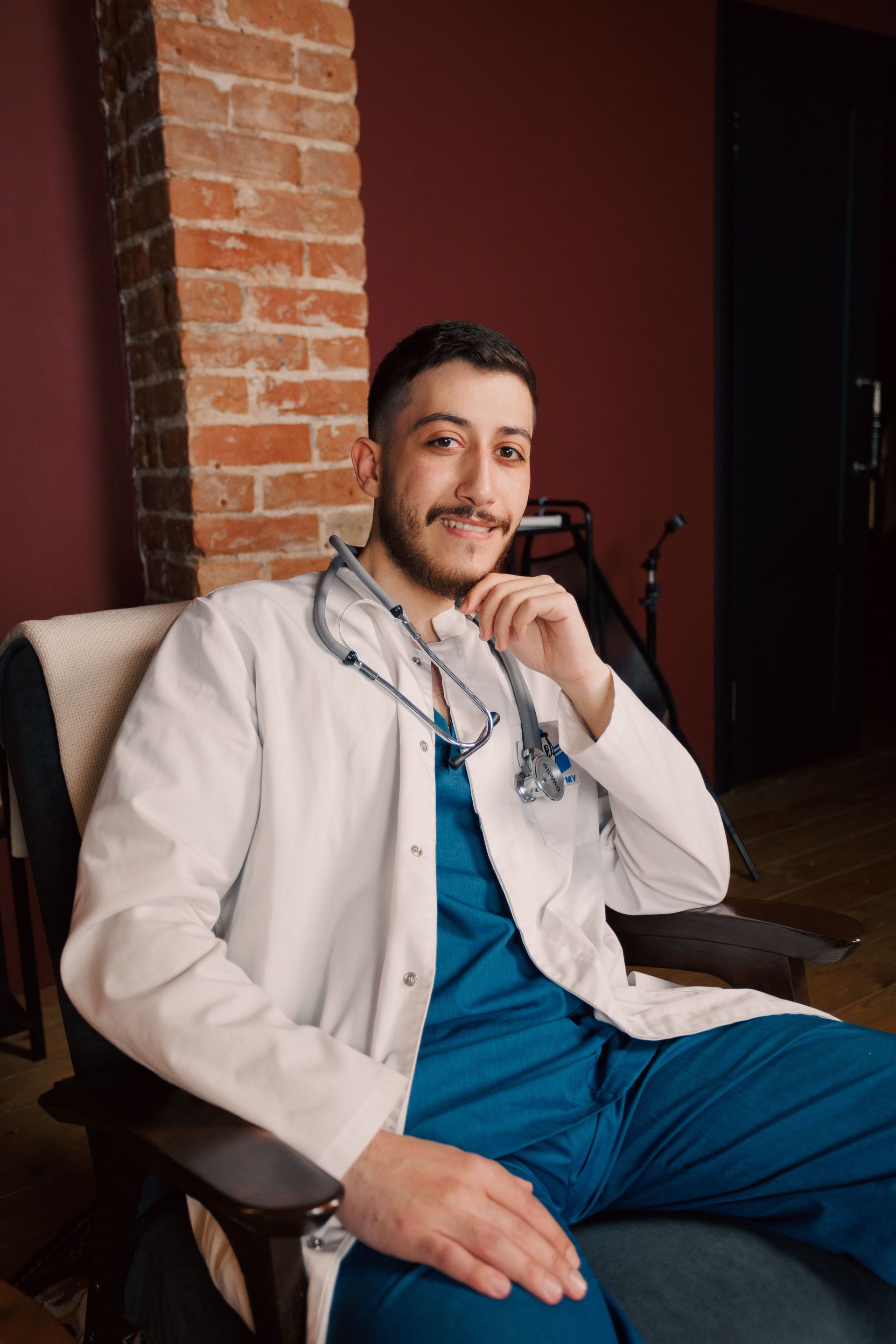 A smiling healthcare professional wearing a white coat and stethoscope speaks with a patient in an office setting.