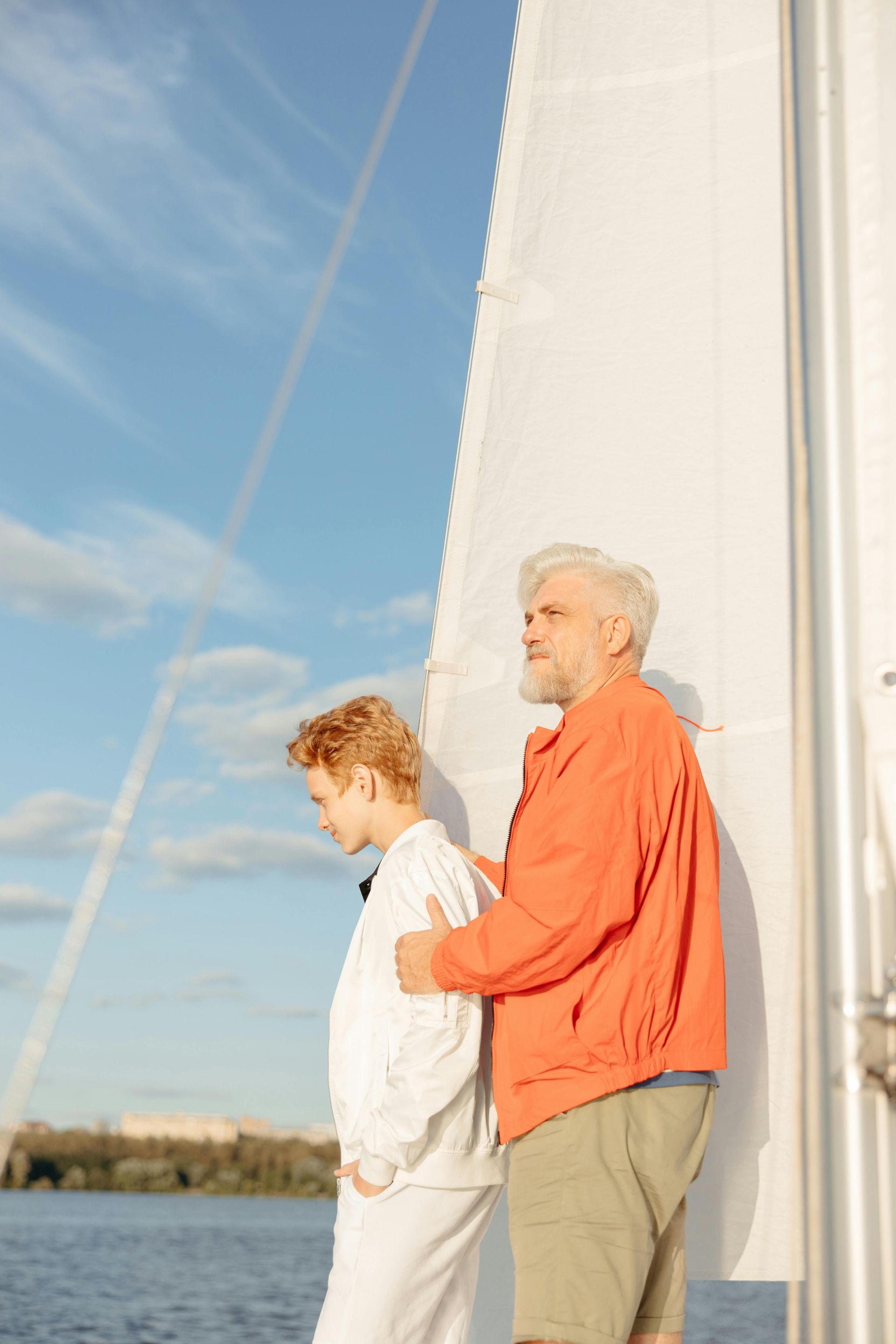 Two people stand on a sailboat, looking out over the water in the golden light of sunset.