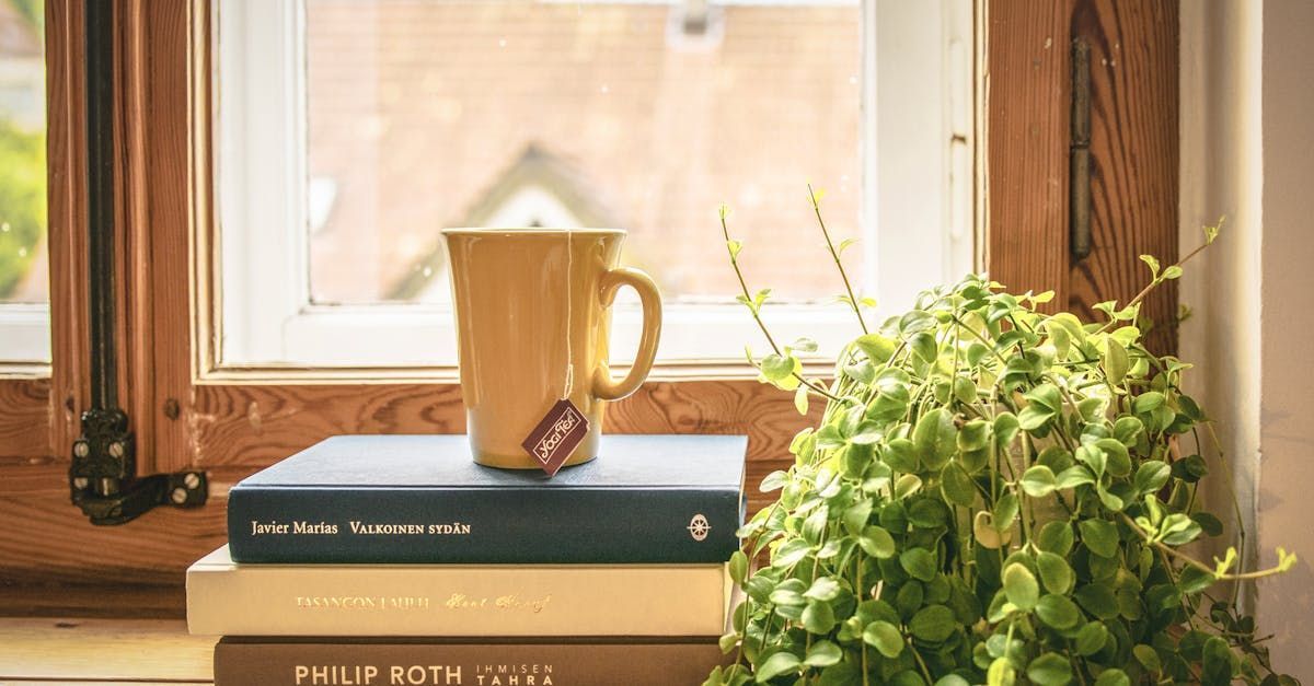 A cup of coffee is sitting on top of a stack of books next to a plant.