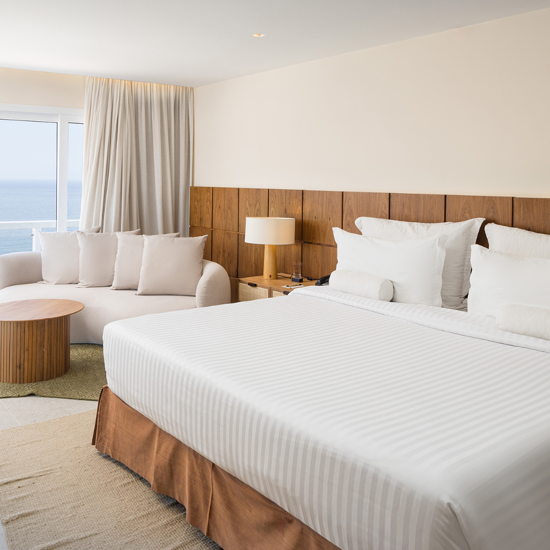 Interior de quarto de hotel com cama, sofá e vista para o mar; logotipo do Othon Palace Rio sobreposto.