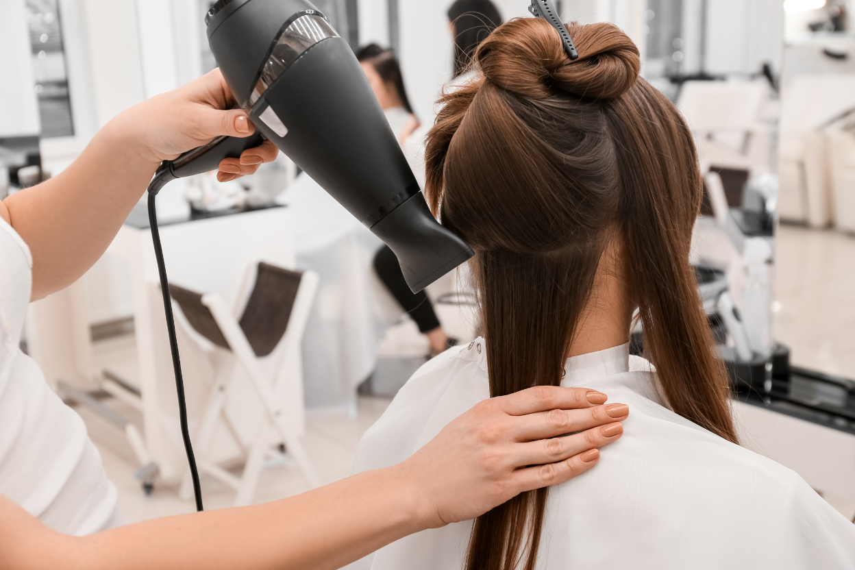 Cabeleireira secando o cabelo comprido e castanho de uma cliente em um salão de beleza.