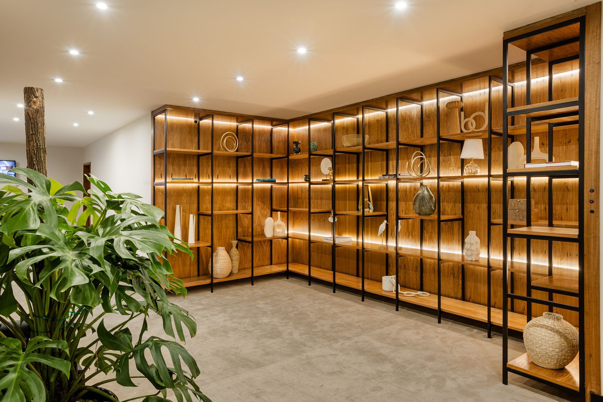 Estante de madeira com iluminação de fundo, exibindo objetos decorativos em uma sala moderna. Othon