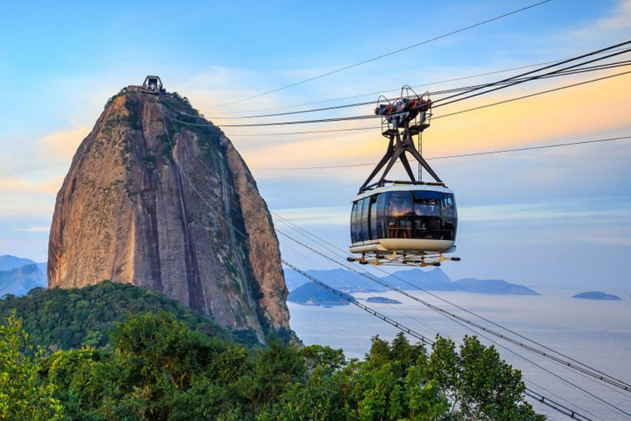 Teleférico subindo o Pão de Açúcar, Rio de Janeiro. Dia claro, céu azul, vista panorâmica do oceano.