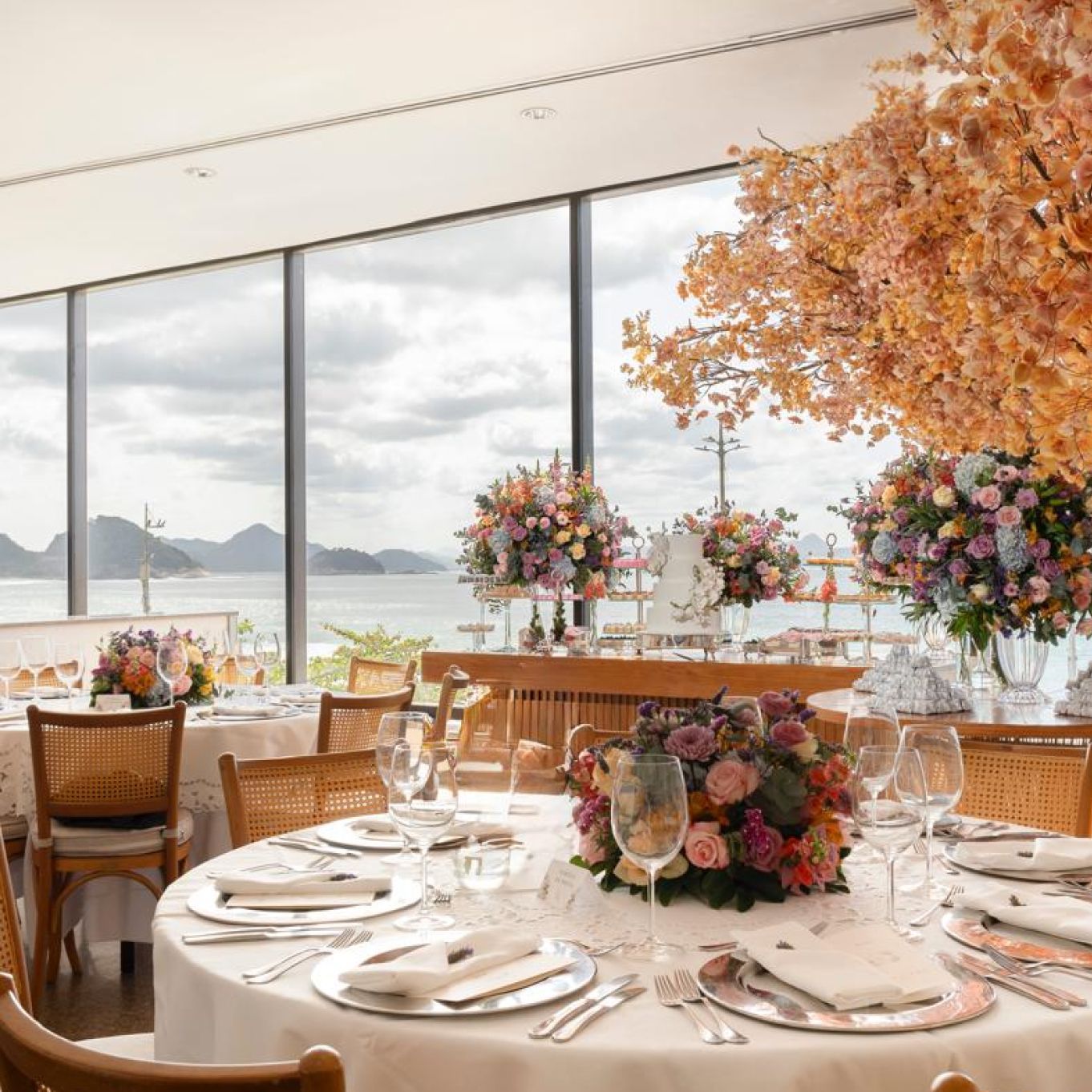 Elegante salão de banquetes com arranjos florais, mesas redondas para convidados e uma vista panorâmica do mar. Othon