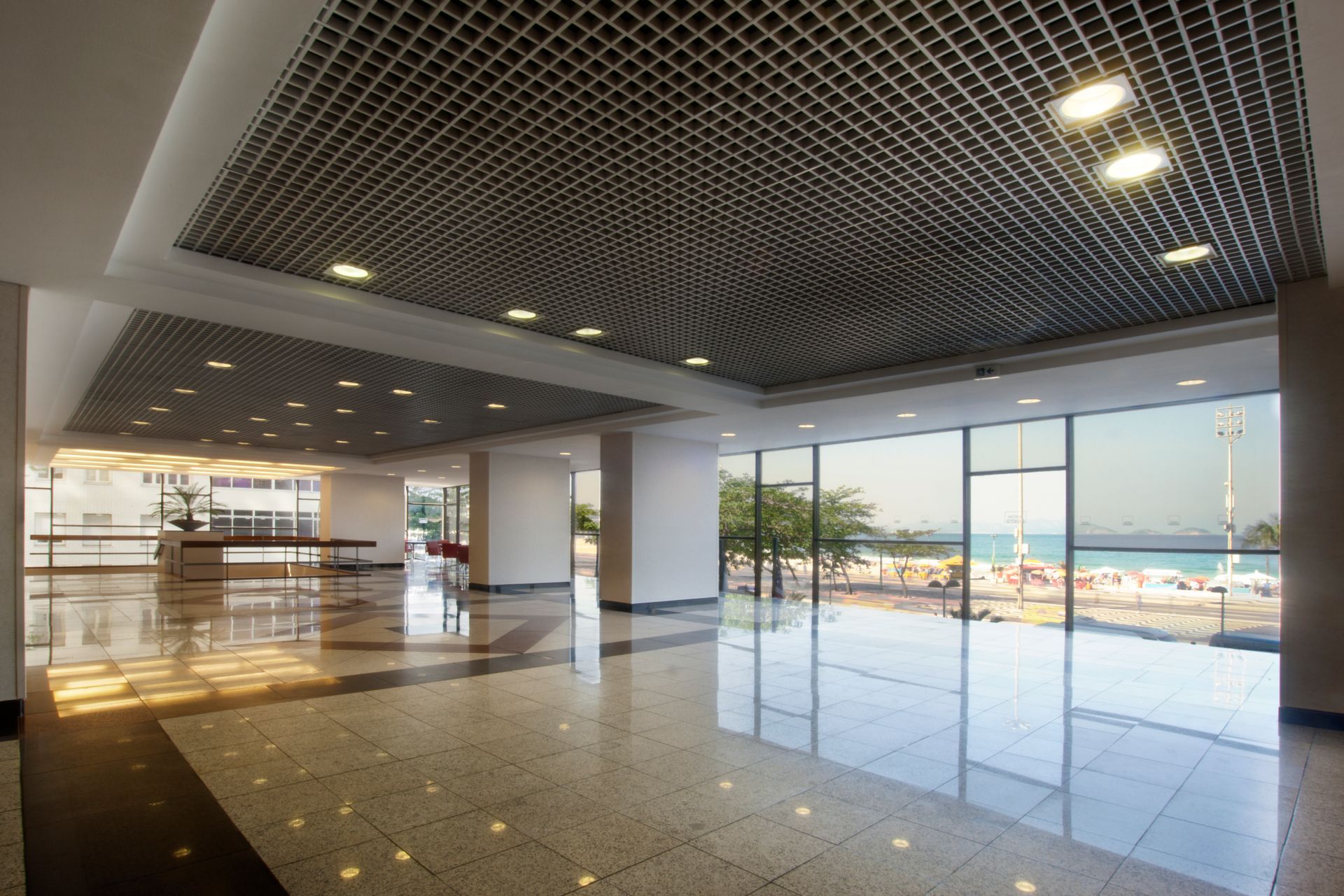 Amplo lobby com teto de grade, janelas do chão ao teto com vista para a praia e piso de cerâmica brilhante. Othon