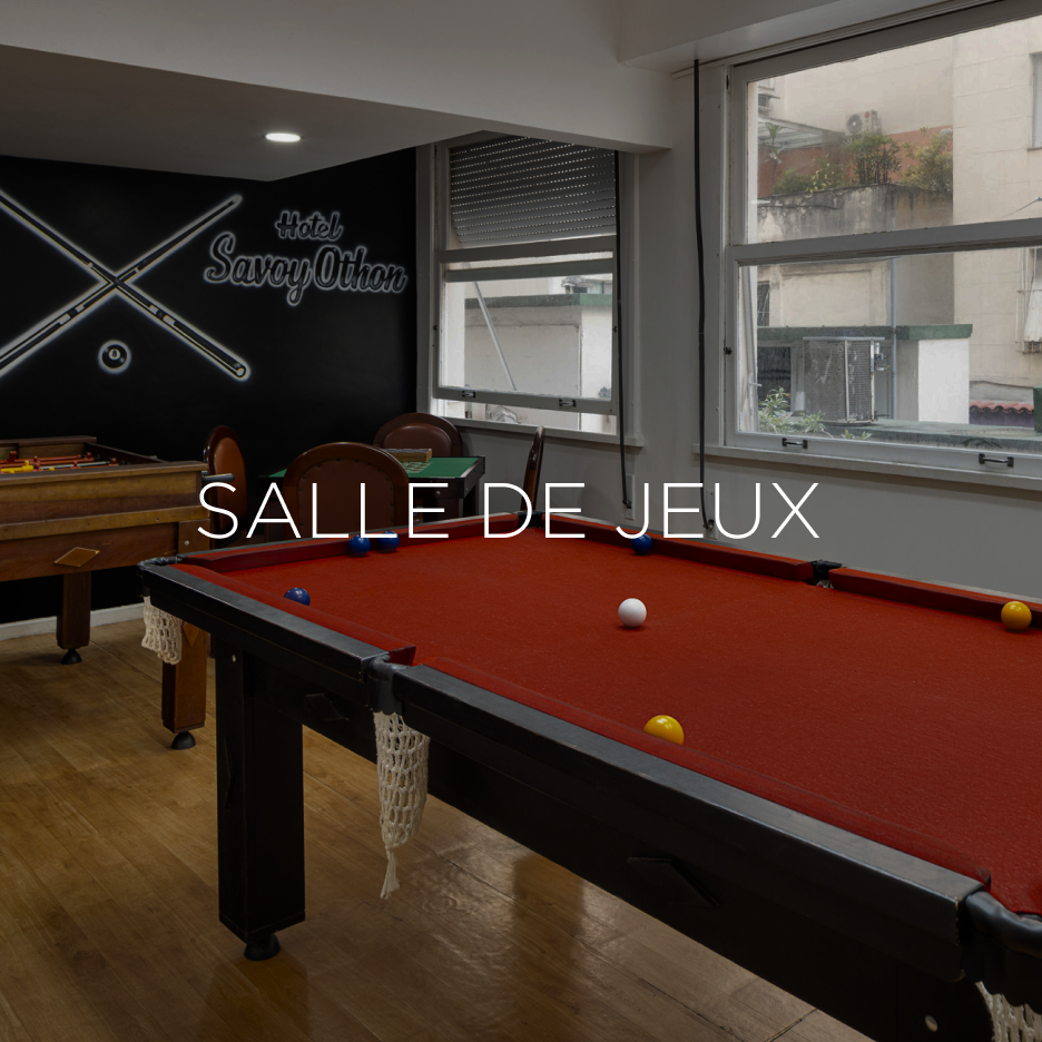 Mesa de bilhar em uma sala de jogos com paredes escuras e janelas. Texto 