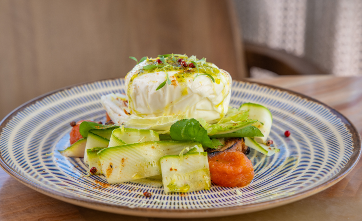 Salada de queijo burrata: uma grande bola de queijo branco, tiras de abobrinha verde e tomates em um prato estampado.