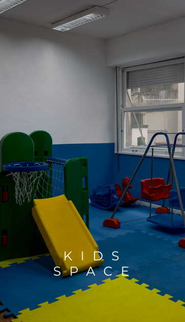 Sala de jogos com escorregador amarelo, cesta de basquete e balanços sobre tapetes azuis e amarelos. Texto