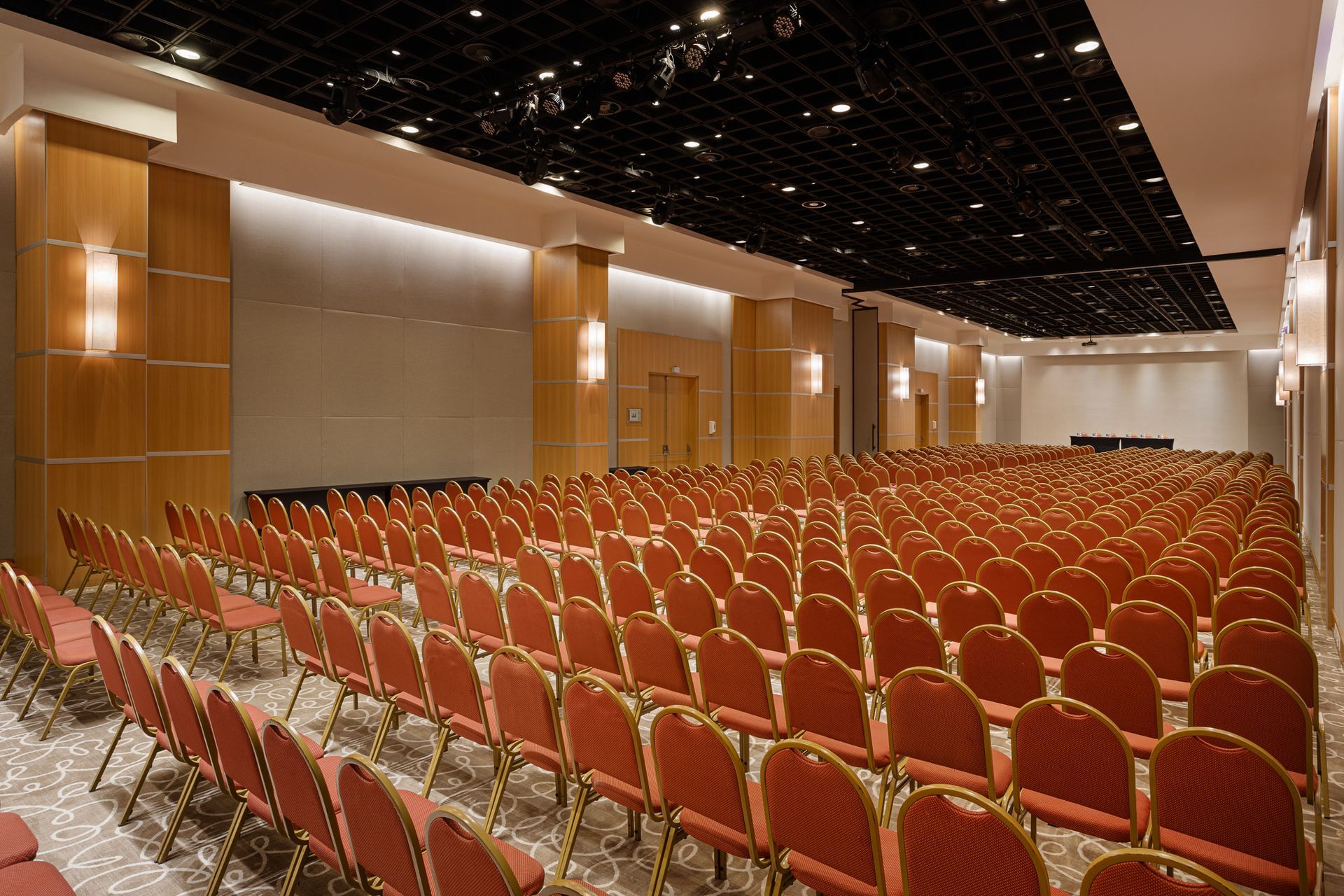 Sala de conferências vazia com fileiras de cadeiras vermelhas, painéis de madeira e teto escuro. Othon