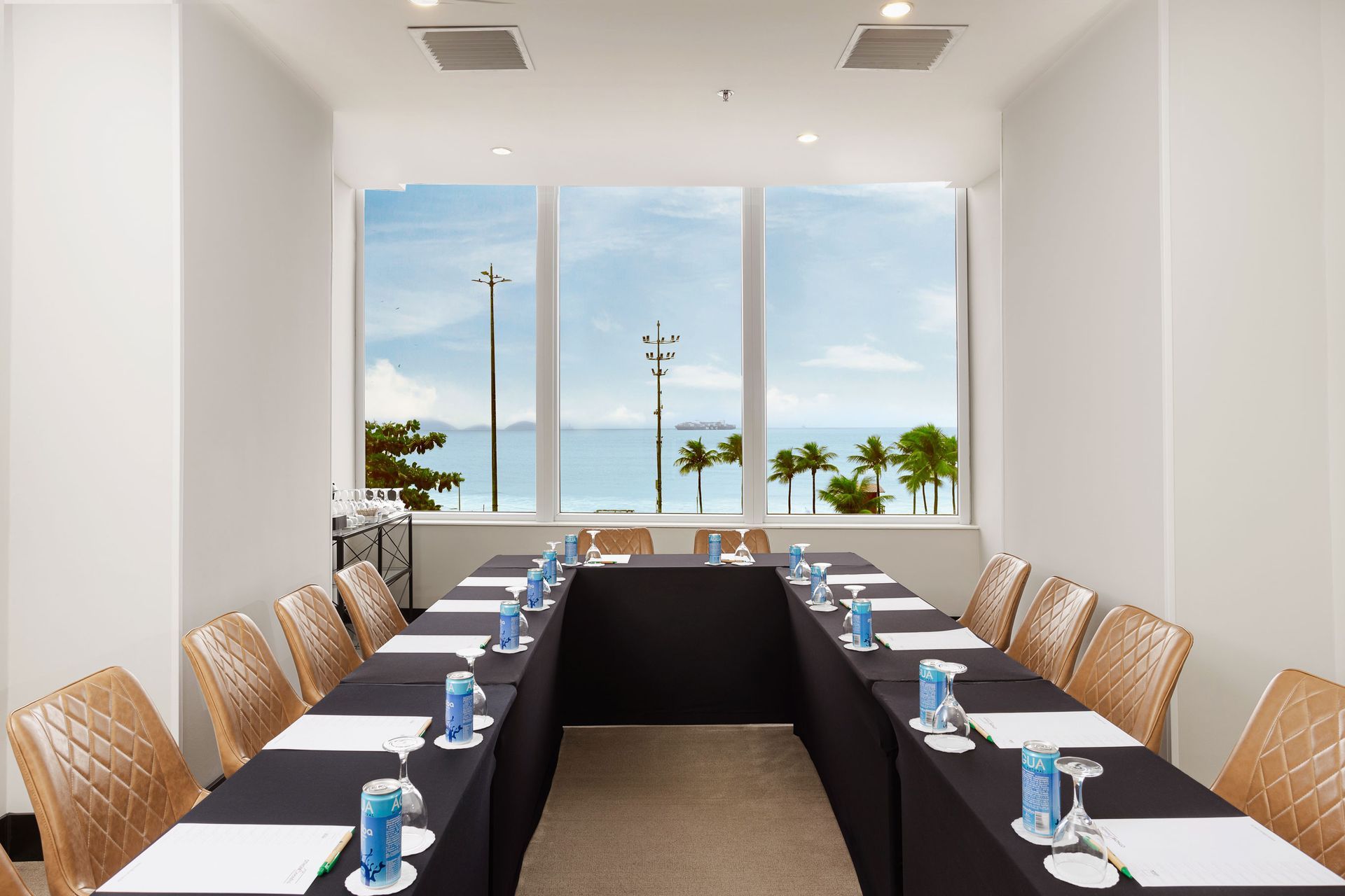 Sala de conferências com mesa em formato de U para reuniões. Vista para o mar pela janela. Othon