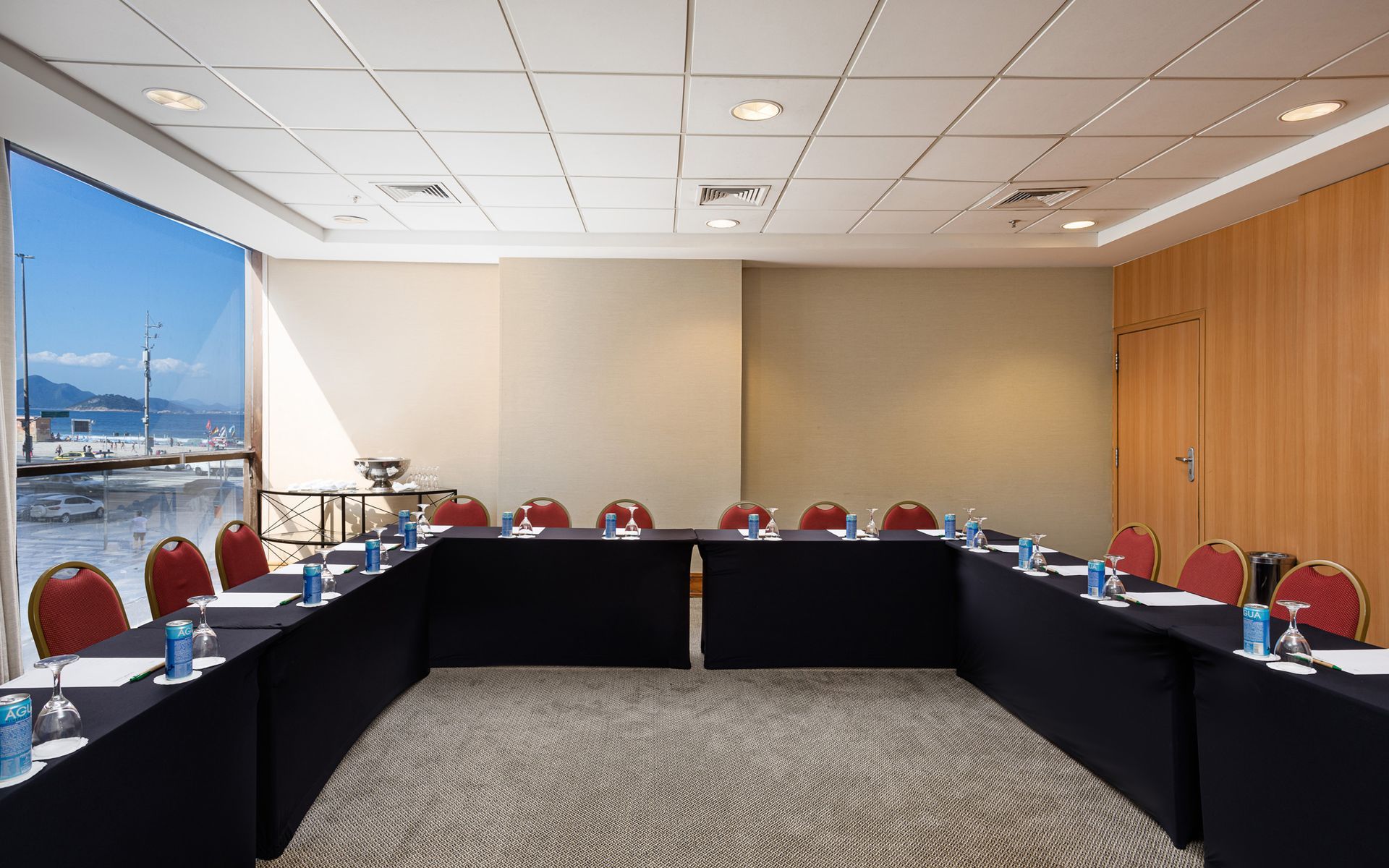 Sala de conferências disposta em formato de U, com vista para a água e cadeiras ao redor de uma mesa preta. Othon