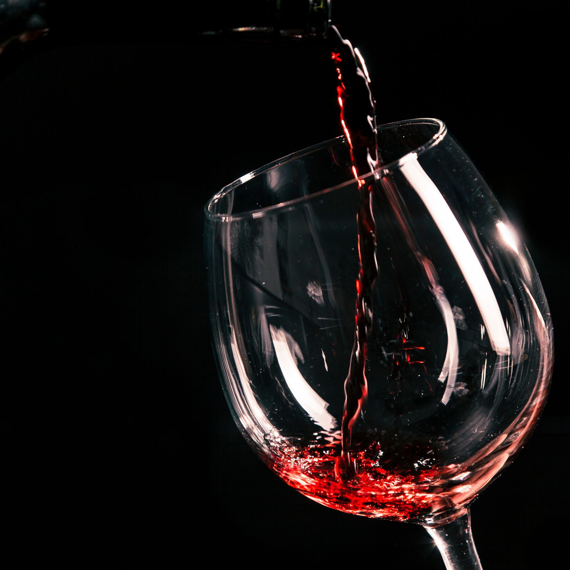 Vinho tinto sendo servido em um copo transparente contra um fundo preto.