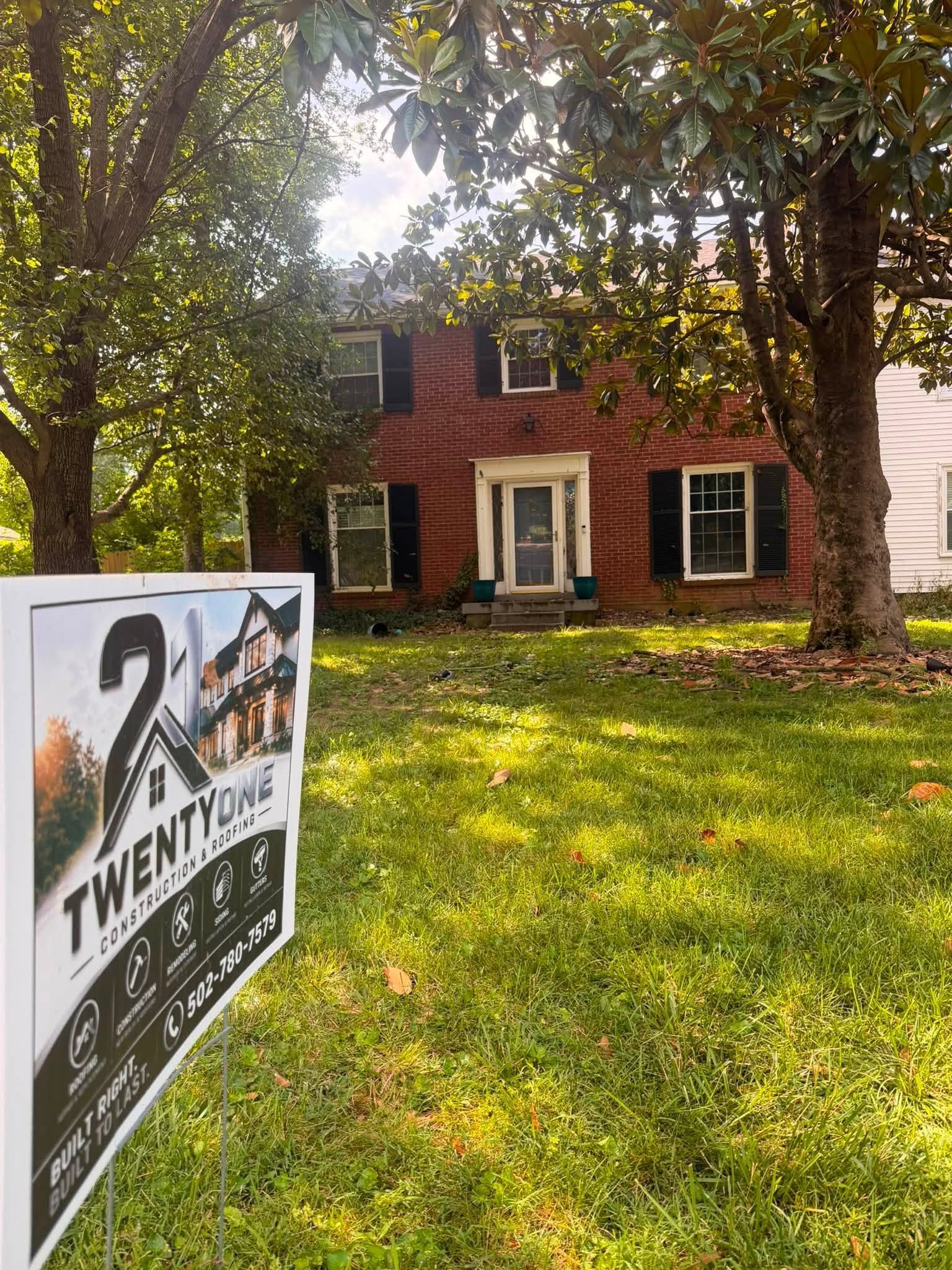 For Sale sign in front of a red brick house with trees and a grassy yard