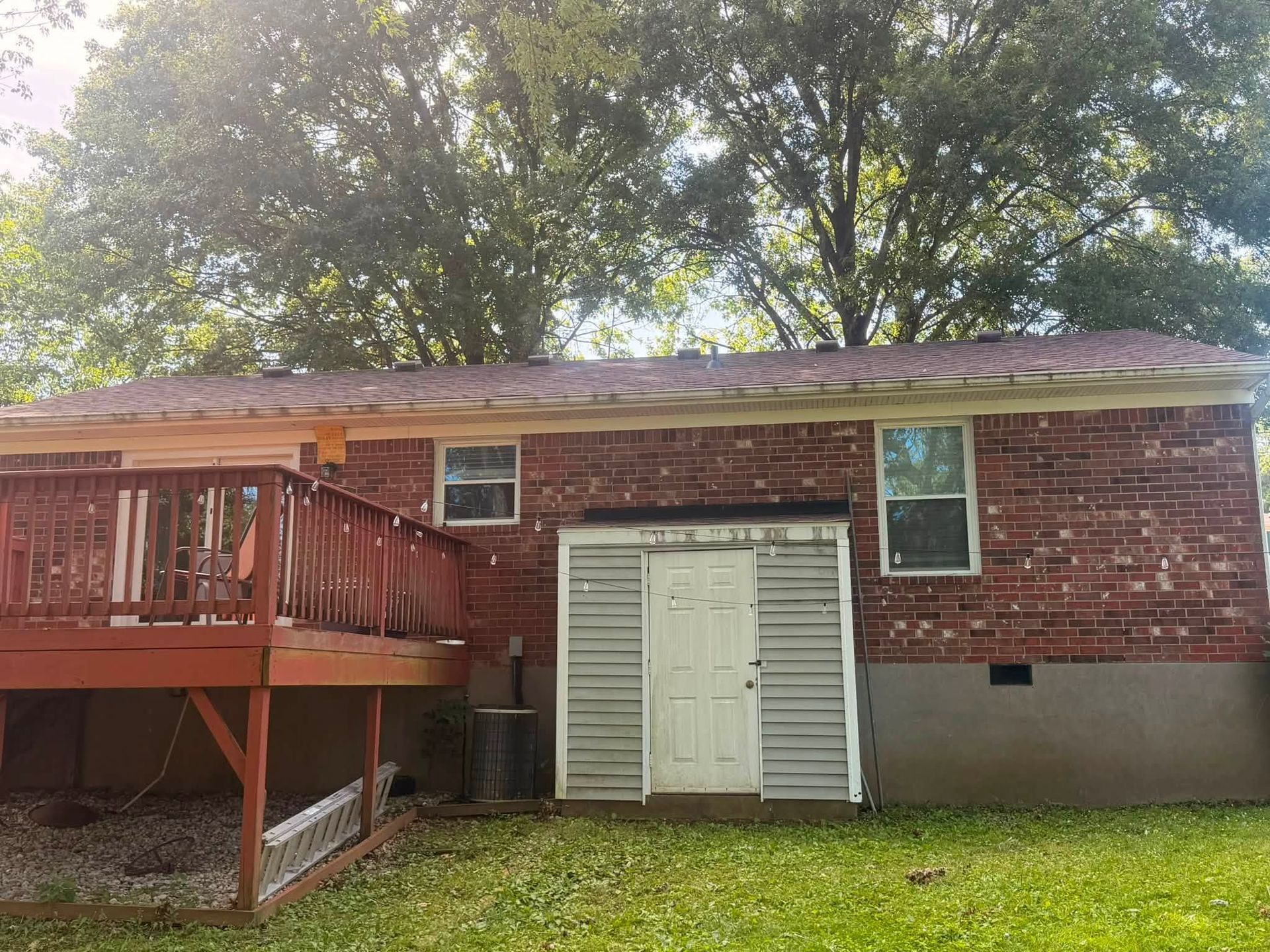 Red brick house with a wooden deck, white double doors, and trees overhead.