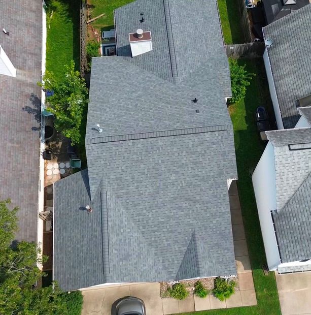 Aerial view of a house with a gray roof, driveway, and small yard bordered by neighboring homes.