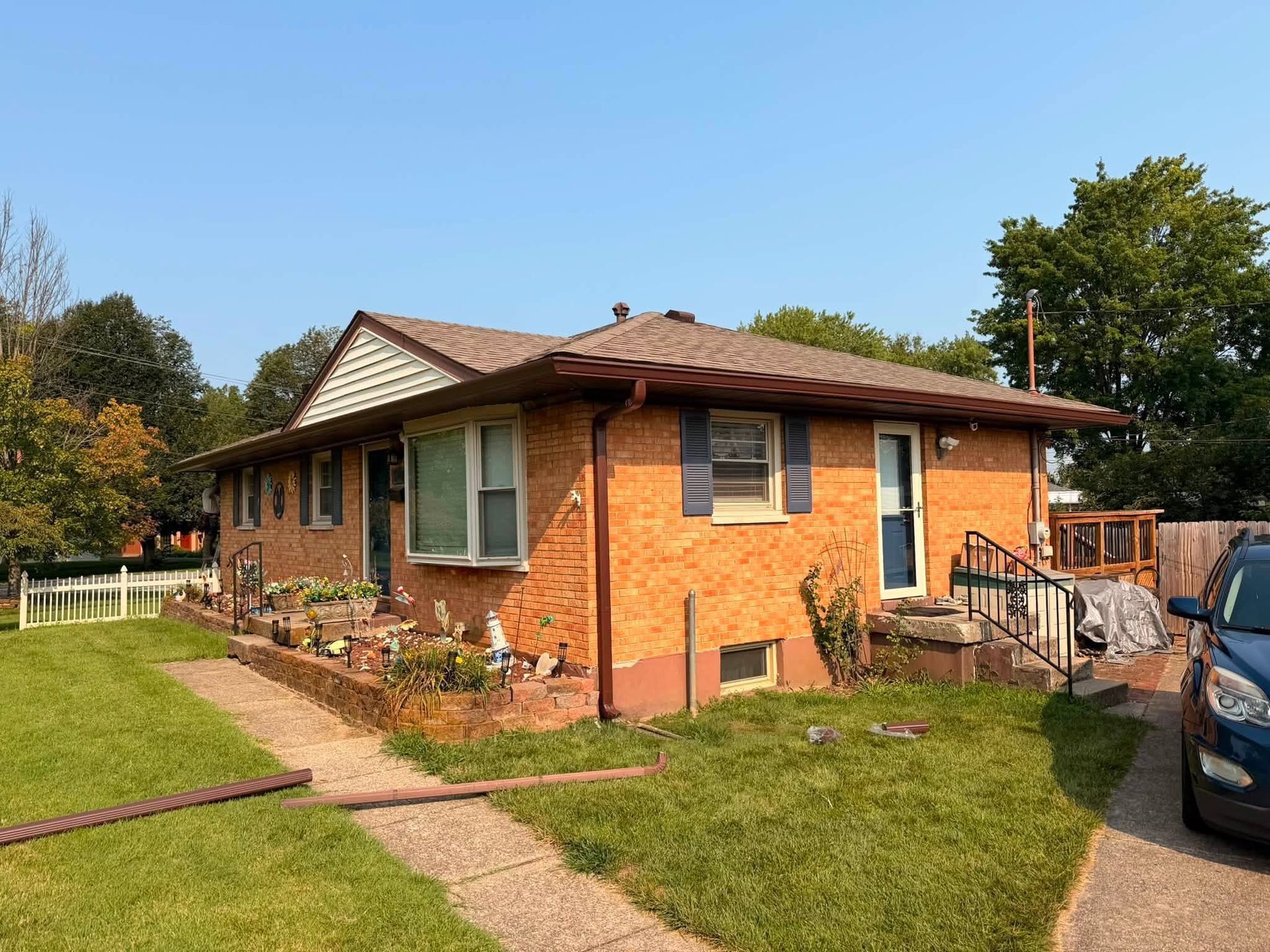 Single-story orange brick house with a front lawn, sidewalk, and parked car beside it.