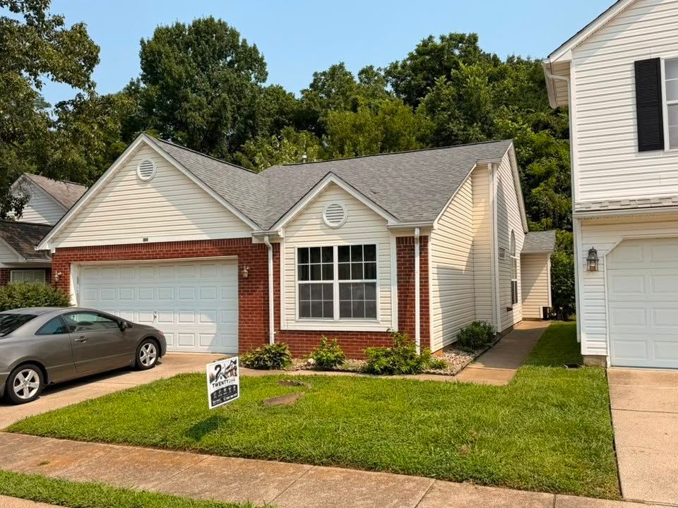 Small brick-and-beige suburban house with a garage, front lawn, and parked car in the driveway.