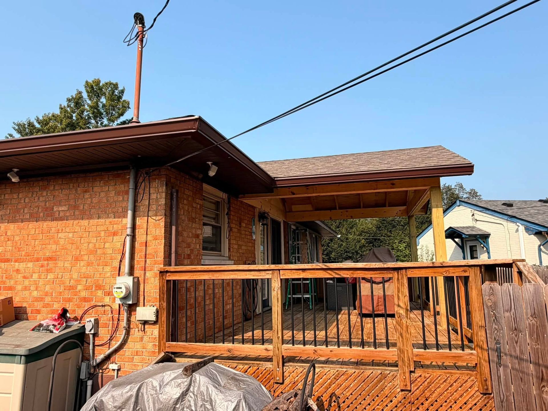 Backyard deck beside a brick house with a wooden railing and utility lines overhead.