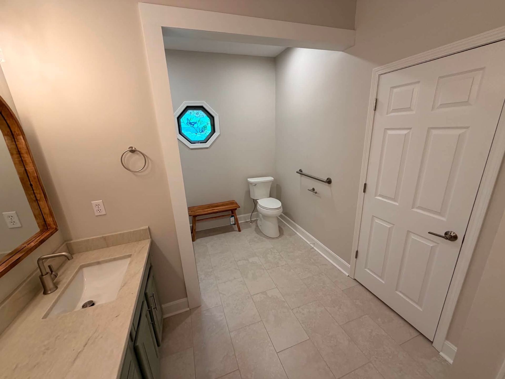 Bathroom with white tile, toilet, bench, towel bar, and a blue octagonal window.