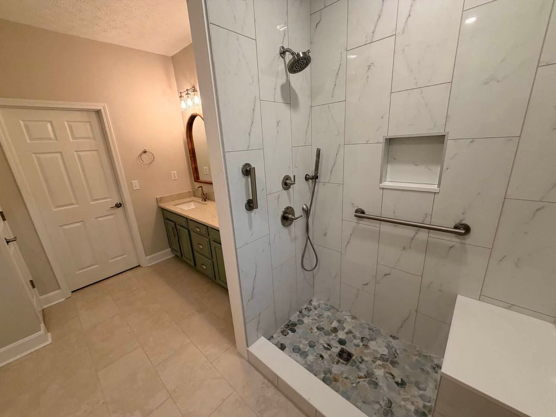 Bathroom with walk-in shower, marble-look tile, glass door, and vanity beside a closed door.