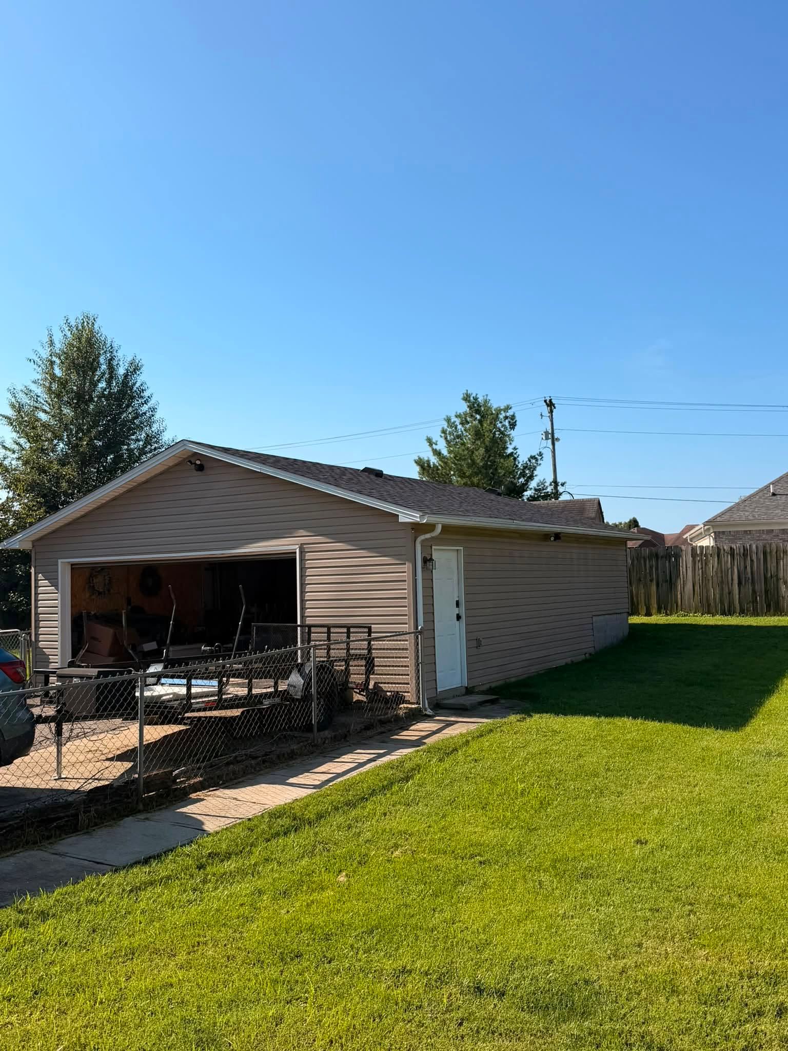 Detached garage with open doors, patio furniture, and a bright green lawn under a blue sky