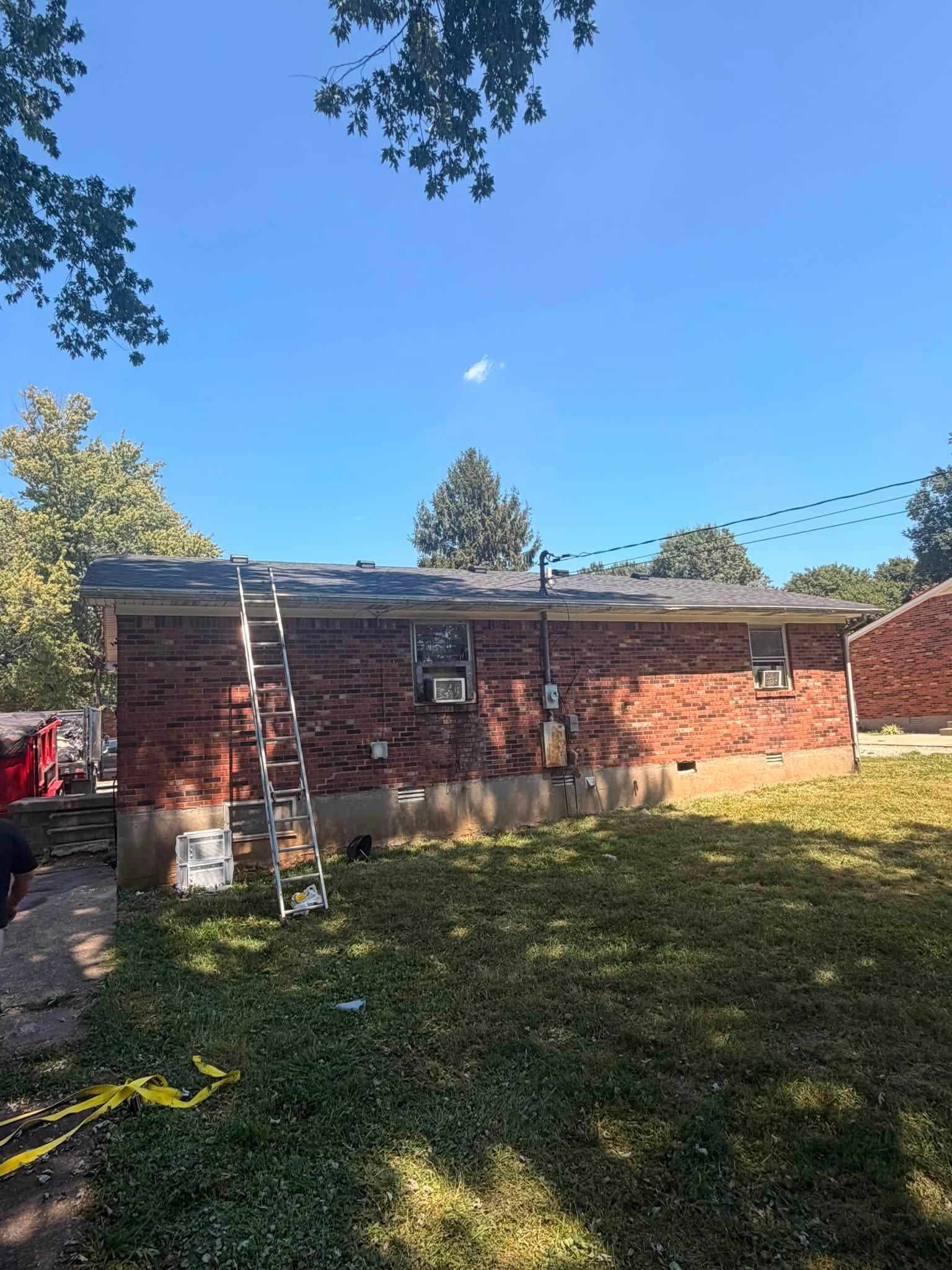 Backyard with a brick shed under repair, ladder leaning against it, and a grassy lawn in sunlight.