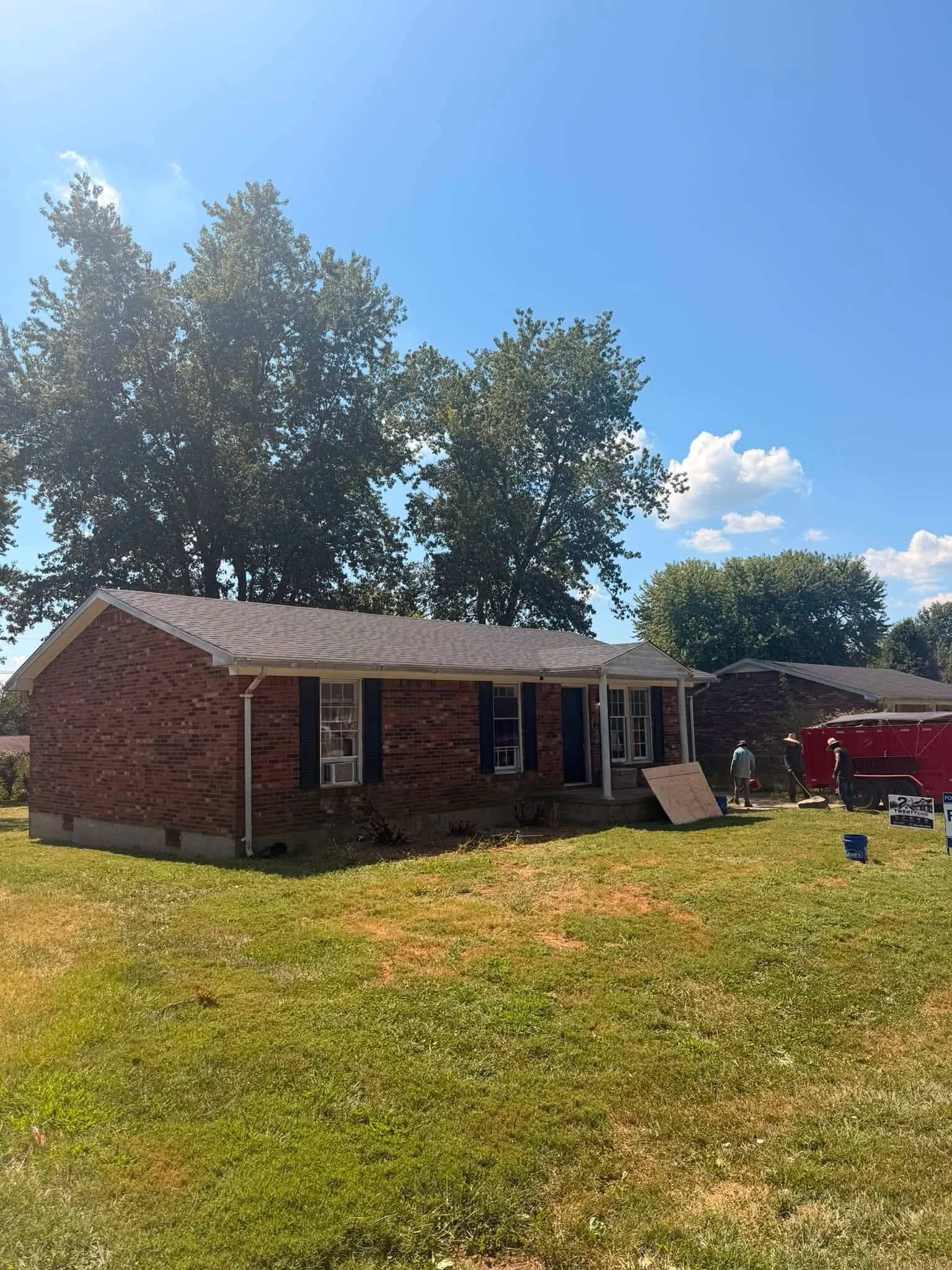 Brick house with a porch on a sunny grassy lawn under a blue sky