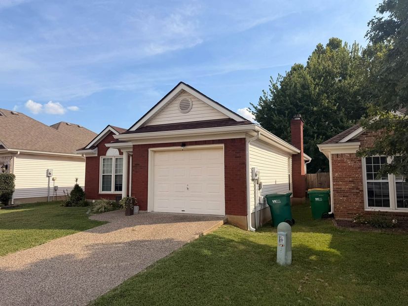 Suburban house with white garage door, brick accents, gravel driveway, and green trash bins