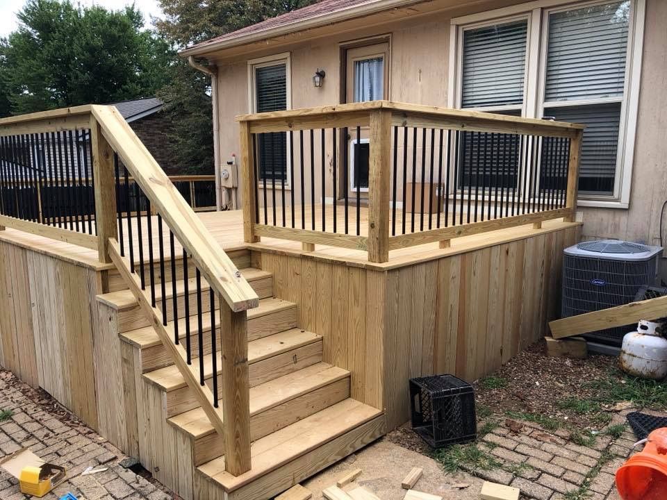 Wooden backyard deck with stairs, railings, and a ramp beside a house.