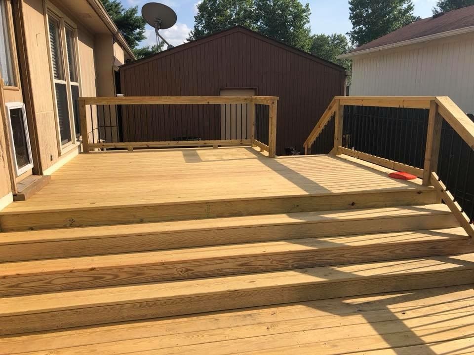 Wooden backyard deck with steps and railing, leading to a shed and fenced yard.