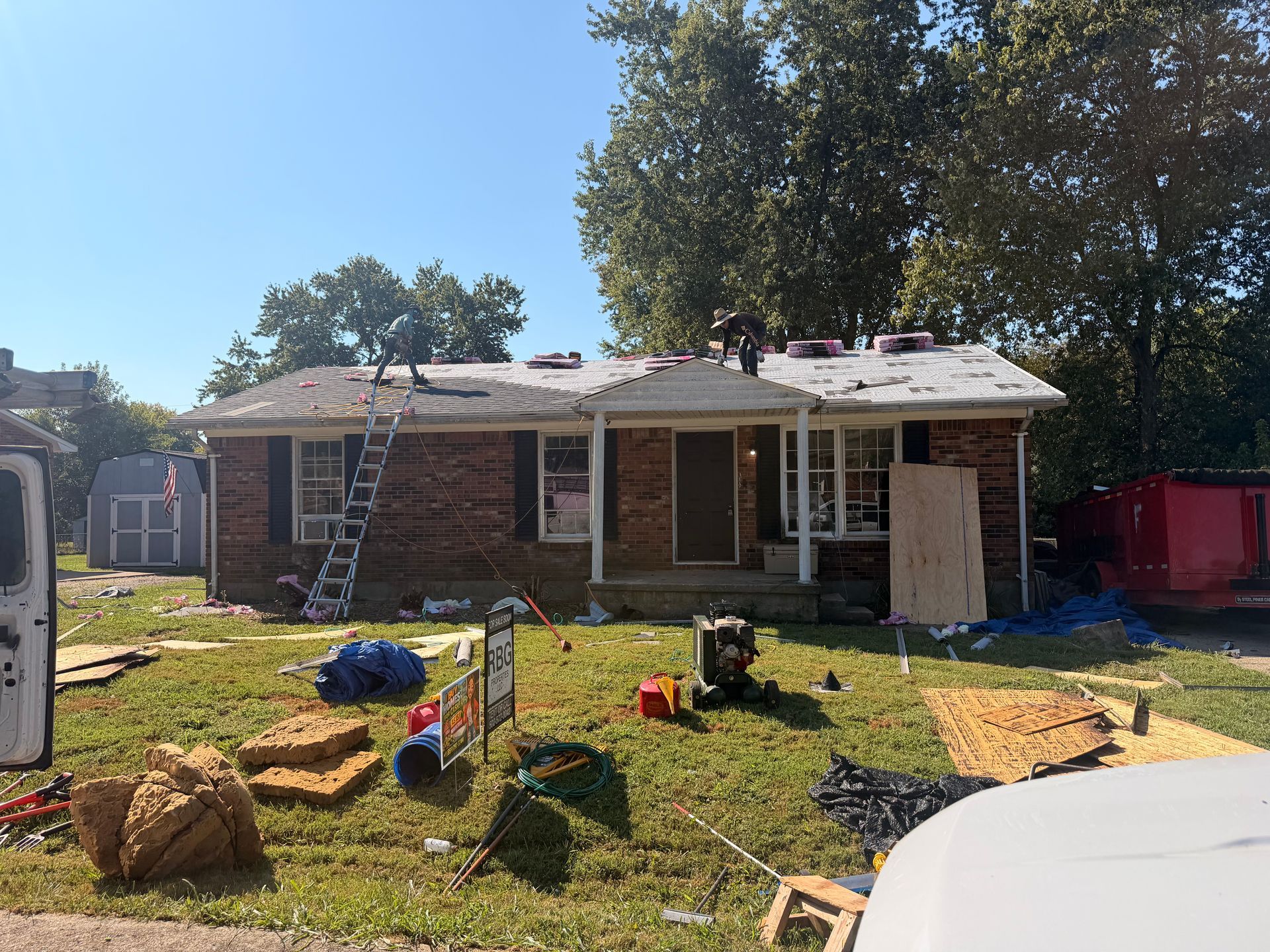 Brick house with roof damage, ladder, and debris scattered across the front yard after a storm