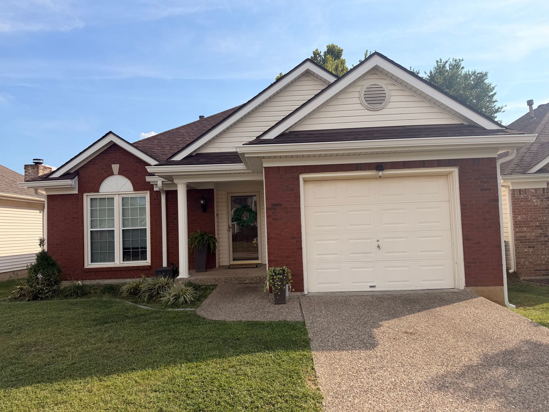 Single-story brick house with red trim, white garage door, and gravel driveway
