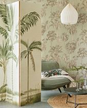 Room with a palm tree screen and green wallpaper, a green chair, and a pendant light.