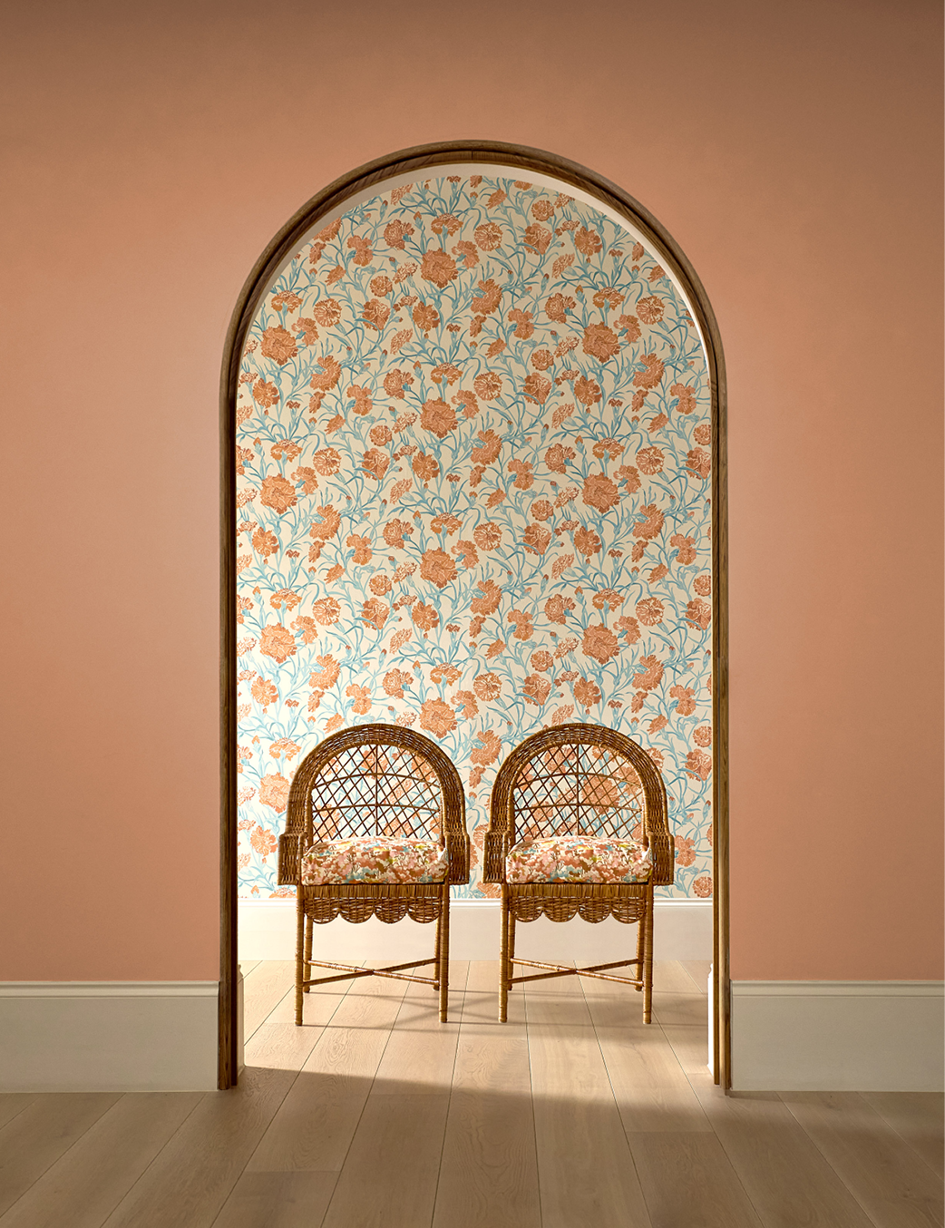 Two wicker chairs sit in an alcove with floral wallpaper. Peach walls frame the opening.