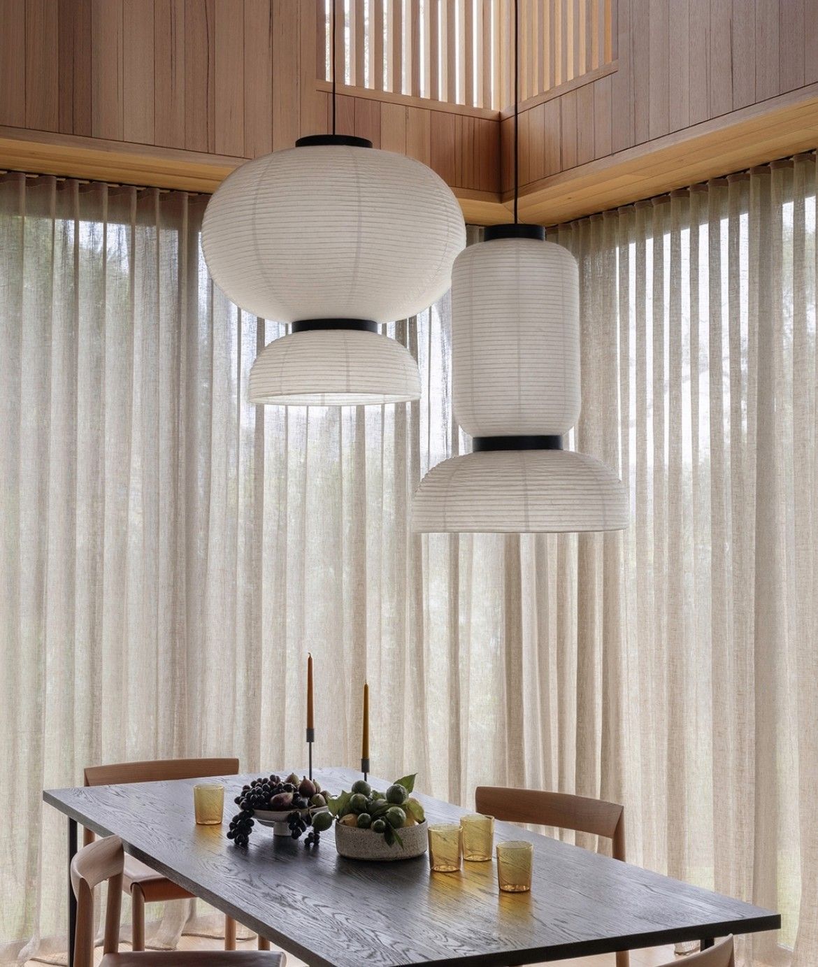 Dining room with paper pendant lamps, long table, chairs, and sheer curtains.