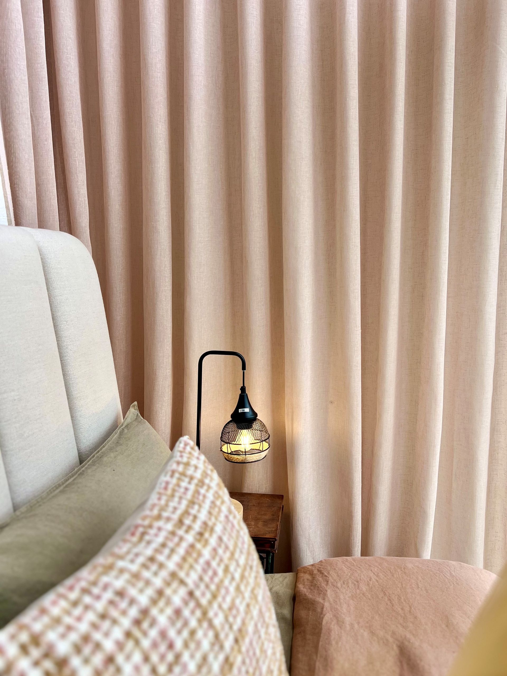Bed with pillows, bedside lamp, and light pink curtains.