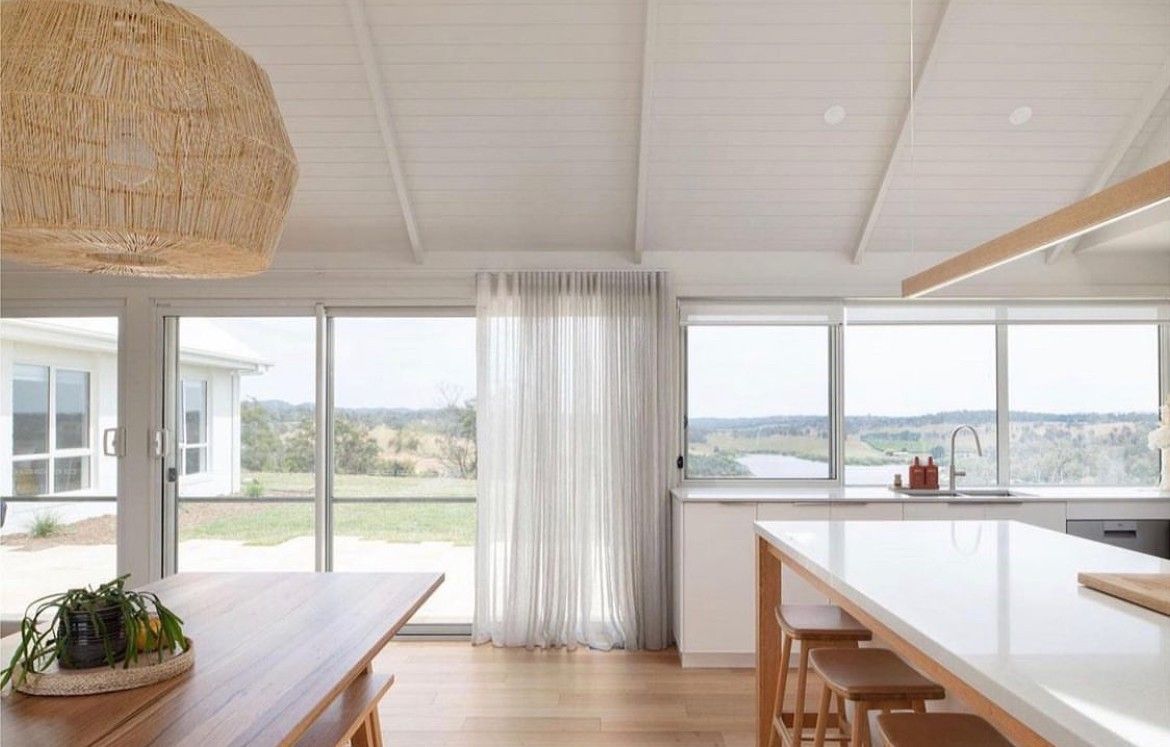 Bright kitchen with white walls, large windows, wooden table, and natural light.