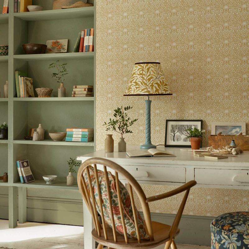 Desk with lamp, chair, and bookshelf in a room with floral wallpaper and green shelving.
