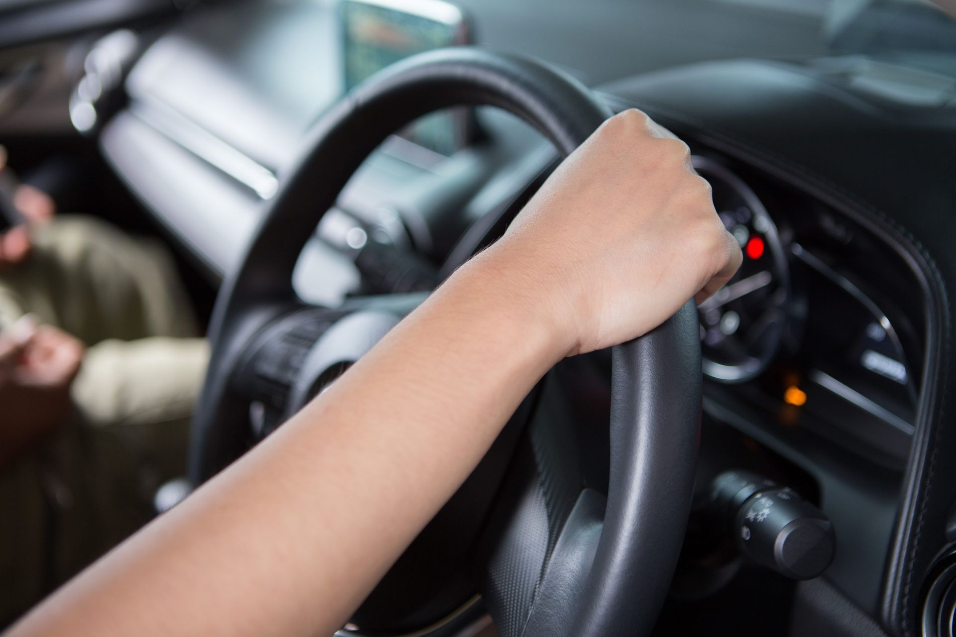 A close-up view of a hand gripping a car steering wheel inside a vehicle cockpit.