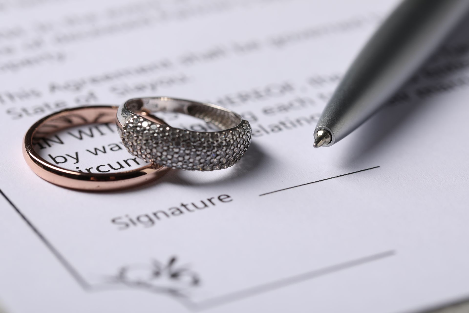 Wedding rings on a marriage contract next to a pen, ready to sign.