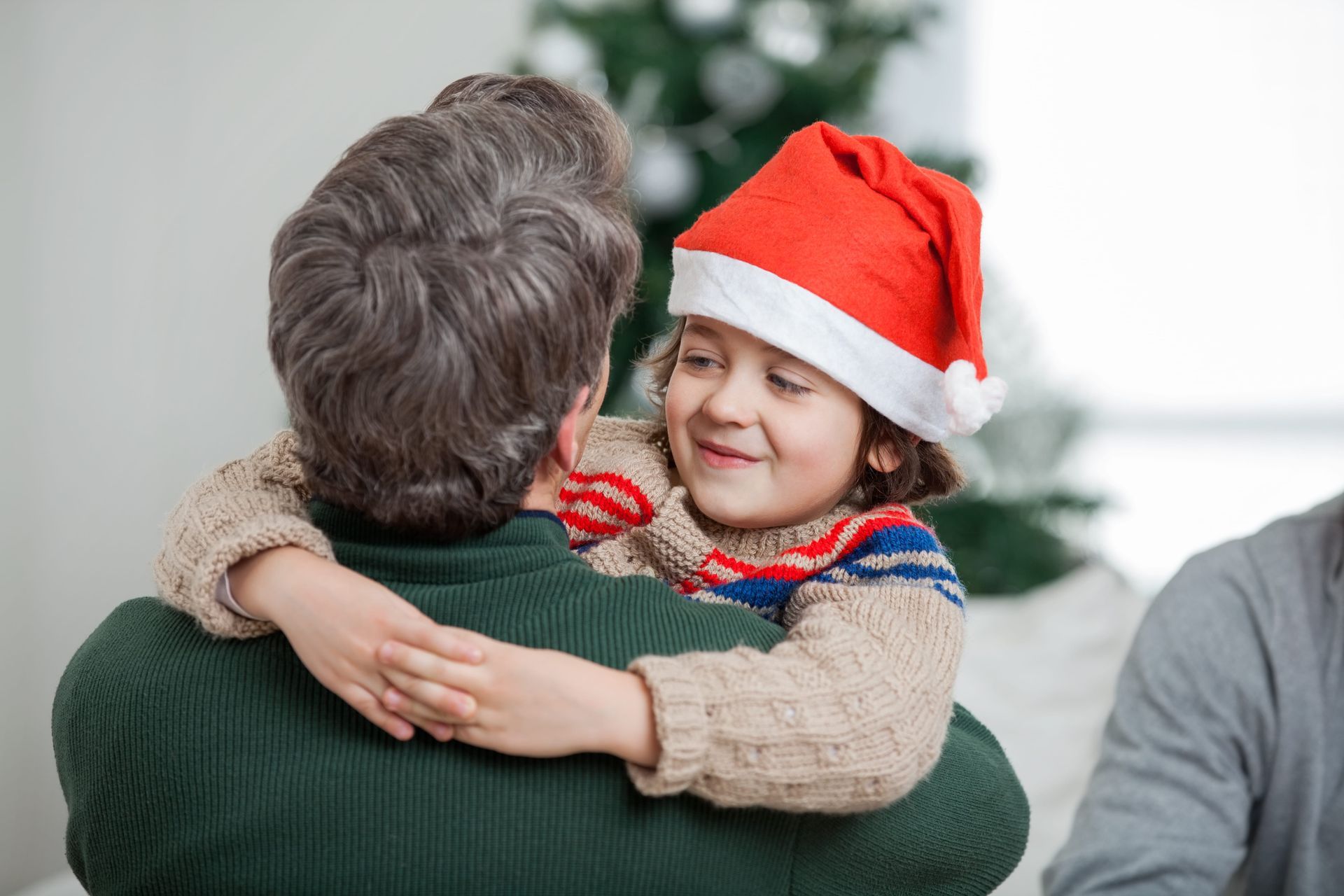 Person in red Santa hat hugging another person indoors near a Christmas tree